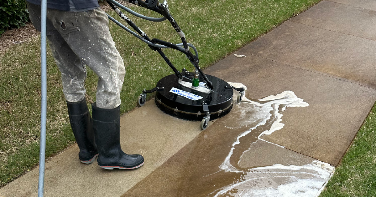 A person is pressure cleaning a sidewalk